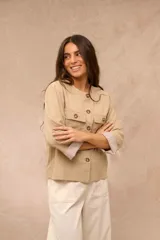 Campera ligera color beige, de cuello redondo y manga larga con puños vueltos de tela a rayas. Cuenta con cierre frontal de botones y dos bolsillos con solapa en el pecho.