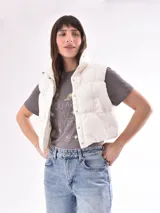 Chaleco puffer corto color blanco con cuello alto y cierre con botones a presión.