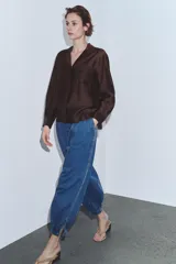 Camisa de manga larga color marrón oscuro, con cuello solapa, escote pico y bajo asimétrico. Presenta un bolsillo plastrón en el delantero con bordado combinado a tono.