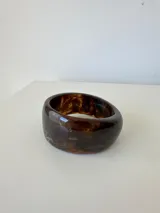 Pulsera rígida tipo brazalete de acrílico con diseño jaspeado en tonos marrones.