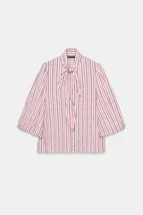 Camisa de rayas verticales rojas, blancas y azules, con cuello alto decorado con lazada, mangas abullonadas por debajo del codo y cierre frontal de botones forrados.
