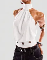 Top halter color blanco, con cuello alto, espalda descubierta y diseño fluido. Cuenta con cintura ajustada y detalle de ojales metálicos.