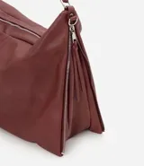 Bolso tipo hobo de gran tamaño en color bordó, confeccionado en poliuretano. Presenta una estructura desestructurada, cierre superior, correas dobles (una de mano y una larga desmontable) y cierres laterales decorativos con tiradores.