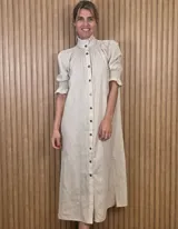 Vestido midi de lino color beige, con cuello alto mao con volado, mangas cortas abullonadas con puños fruncidos y cierre frontal completo con botones.