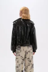 Chaqueta corta de cuero sintético negro con cuello camisero, cierre frontal con cremallera, bolsillos laterales y mangas largas abullonadas.