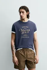 Camiseta de corte relajado, color azul marino, con cuello redondo y manga corta. Presenta un estampado frontal con texto y diseño en tono dorado con efecto desgastado.