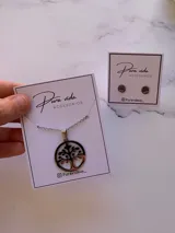 Conjunto de collar y aros de acero quirúrgico con diseño de árbol de la vida. El collar presenta un dije circular calado y los aros son tipo botón.