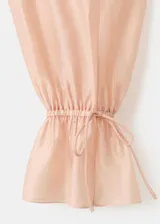 Blusa de seda color rosa pálido con volados frontales, cuello redondo y mangas largas con puños elásticos.