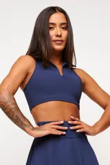 Top deportivo negro, estilo crop top, con cuello polo y escote en V. Presenta tirantes anchos y corte ajustado al cuerpo.