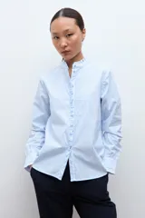 Camisa de manga larga a rayas celestes y blancas, con cuello mao y volados verticales en el frente.