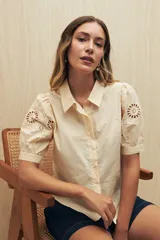 Camisa color crema o amarillo muy pálido, con cuello clásico y mangas cortas abullonadas que presentan bordados calados florales (broderie anglaise).