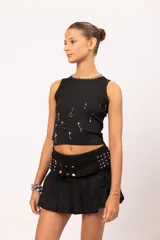 Pollera mini tableada de color negro, con diseño de tiro medio. Presenta un cinturón ancho integrado con apliques de tachas plateadas y cierre de doble botón metálico.