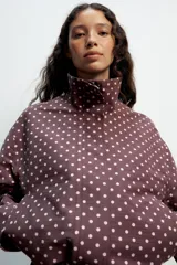 Cazadora negra con estampado de lunares blancos, cuello subido, manga larga, bolsillos delanteros, bajo ajustable con cordones y cierre frontal con cremallera y solapa con botones ocultos.