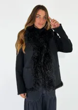 Chaleco de denim negro con detalles de piel sintética en los bordes frontales y el ruedo. Presenta bolsillos frontales tipo parche y un diseño estructurado.