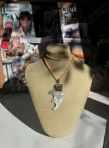 Collar con cordón fino color ocre, dije de nácar blanco con forma irregular y aplique metálico dorado.