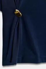 Camiseta de algodón compacto color negro, con cuello redondo, manga corta y detalle de aplique metálico en el frente que genera un ligero fruncido lateral.