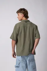 Camisa de manga corta de color verde militar, confeccionada en una mezcla de lino y viscosa. Posee un calce regular, cuello plano y cierre frontal con botones, destacándose por su textura liviana y respirable.