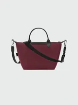 Cartera de mano modelo Le Pliage Energy de Longchamp, tamaño pequeño. Confeccionada en lona de color bordó con detalles en cuero negro, incluyendo solapa frontal con cierre de botón a presión y asas cortas. Incluye correa de hombro ajustable y extraíble de tejido técnico negro.