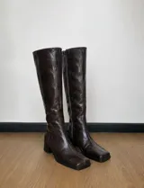 Botas de caña alta confeccionadas en 100 cuero color marrón oscuro con acabado texturizado efecto arrugado, punta cuadrada y taco bloque. Poseen cierre lateral interno.