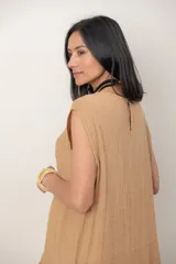 Vestido midi de lino color beige, sin mangas y con cuello redondo. Cuenta con un diseño irregular con detalle de volado vertical a un costado.