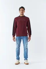 Buzo color bordó con cuello redondo y mangas largas con detalle de franja negra en los hombros. Tiene puños y logo "Mistral" estampado en relieve en el pecho.