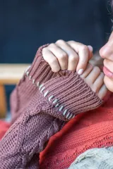 Sweater de punto con diseño de ochos y estilo patchwork, combinando paneles en colores terracota, marrón y beige. Presenta cuello redondo, mangas largas y costuras decorativas a la vista.