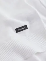 Sweater de punto blanco con textura slub (tejido irregular), cuello redondo, hombros caídos y puños y bajo acanalados. Presenta una pequeña etiqueta con logo de goma en el bajo.