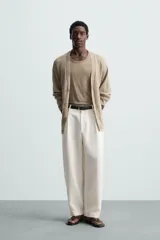 Pantalón blanco de corte relajado (relaxed fit) con pliegues frontales, bolsillos laterales y bolsillos traseros de vivo. Cierre frontal con cremallera y botón.