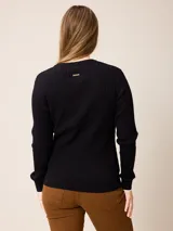 Sweater de punto con diseño de trenzas verticales, color negro, con cuello redondo, mangas largas y puños con detalle en contraste blanco. Presenta un pequeño logo bordado en el pecho.