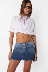 Minifalda de jean azul con lavado degradé, tiro medio con doble cintura, bolsillos delanteros y traseros, cierre metálico y dos botones personalizados.