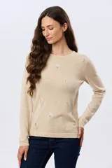 Buzo tejido de algodón color beige, de manga larga, con cuello redondo y delicados motivos bordados distribuidos en la prenda.