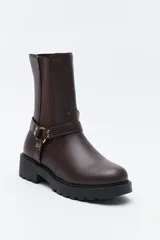 Bota tipo biker de caña media en cuero sintético negro, con panel elástico lateral, suela gruesa dentada y arnés decorativo con herraje metálico.