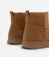 Bota de caña media color marrón, confeccionada en poliéster con acabado suave. Cuenta con interior forrado en piel sintética para mayor abrigo, tirador trasero y suela plana de goma con diseño dentado.