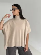 Poncho de tejido de punto color marrón chocolate, con cuello alto tipo polera y mangas cortas amplias. Presenta un diseño holgado con terminaciones acanaladas en el ruedo.