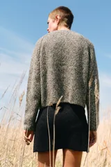 Chaqueta de punto de cuello redondo y manga larga, con textura jaspeada en tonos tierra y azul. Presenta cierre frontal con botones oscuros y dos bolsillos de plastrón en el delantero.