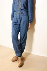 Pantalón de jean azul con diseño de tiro alto, pinzas en la cintura y corte holgado que se estrecha hacia los tobillos.