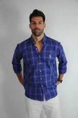 Camisa de manga larga con estampado de cuadros en tonos azules, cuello abotonado y cierre frontal con botones. Presenta un pequeño bordado en el pecho.