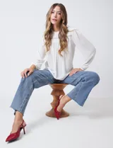 Blusa blanca de gasa con pliegues en la parte delantera y encaje calado en el cuello y el pecho. Cuello a la base con terminación fruncida. Manga larga con puño elastizado. Espalda lisa con abertura tipo gota y botón.