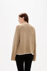 Cardigan de punto color natural, con cuello en V, cierre frontal con botones y diseño holgado. Presenta detalles de costuras decorativas bordadas a lo largo de las mangas y en los bordes.