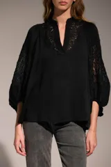 Camisa negra de corte holgado con cuello mao y escote en V. Presenta detalles de encaje en el cuello y en las mangas abullonadas de largo tres cuartos.