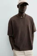Camiseta de corte relajado (relaxed fit) color blanco roto, con cuello redondo y manga corta. Presenta un bordado sutil en el pecho con diseño floral en tonos claros.