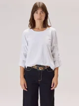 Remera blanca de algodón con cuello redondo y mangas tres cuartos que presentan detalles de pespuntes horizontales y paneles de tela combinada.