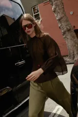 Blusa de cuello subido y manga larga abullonada con puños ajustados. Presenta un diseño semitransparente con textura arrugada y cierre frontal con botones a tono.