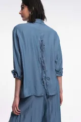 Camisa color marrón de corte oversized, con abotonadura frontal y en las mangas. Presenta un corte vertical en la espalda con lazos decorativos.