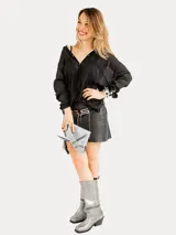 Bota de cuero metalizado plateado con punta cuadrada y tacón bajo. Presenta un diseño versátil con cierre metálico que permite desmontar la polaina superior, transformando la silueta de bota alta a botín.