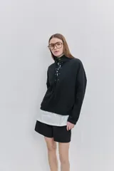 Buzo de algodón negro con calce relajado, cuello alto con cordones cruzados y ojales metálicos, bolsillos laterales y puños y ruedo elásticos.