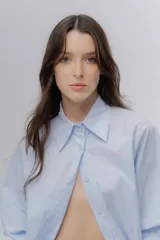 Camisa clásica de algodón con cuello camisero, cierre frontal de botones y mangas largas con puños anchos. Presenta un corte holgado y diseño minimalista.
