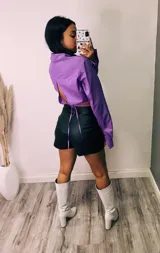 Camisa cropped negra con cuello clásico, mangas largas con puños abotonados y cierre frontal con botones. Presenta detalle de tachas plateadas en el cuello.