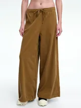 Pantalón de corte holgado y pierna ancha, confeccionado en pana color marrón. Presenta cintura elástica con cordón ajustable y diseño de tiro medio.