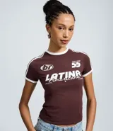 Remera de algodón color bordó con cuello redondo y bordes de mangas en color blanco. Presenta un diseño de estilo deportivo con estampado frontal que incluye el texto 'LATINA' y detalles de rayas blancas en los hombros.